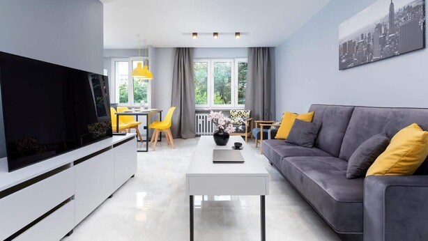 A modern living room with a grey sofa, yellow cushions, a white coffee table, and a flat-screen TV.