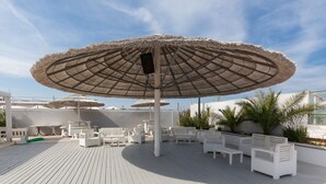 Terraza con sillones blancos, una sombrilla grande y zona junto a la piscina.