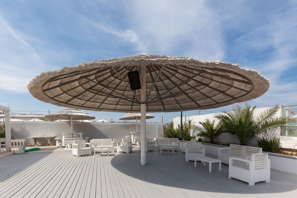 A deck with white lounge chairs, a large umbrella, and a poolside area.