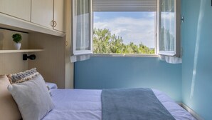 Un dormitorio con cama, ventana con cortinas, estante con planta y vistas a árboles.