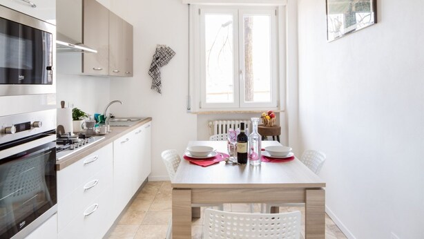 A modern kitchen with white cabinetry, a built-in oven, and a dining area with a table set for two.