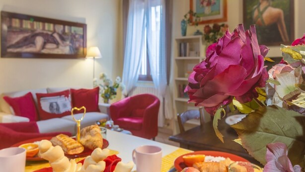 A cozy living room with a dining table set for a meal, a red armchair, and a bookshelf in the background. - Ariostea University Duplex Apartment (Ferrara)