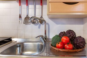 A kitchen with a stainless steel sink, a wooden cabinet above, and a bowl of vegetables on the counter. - Ariostea University Duplex Apartment (Ferrara)