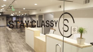 A reception area with a modern design, including a reception desk, a potted plant, and a sign with a logo. - Stay Classy Hostel (San Diego)