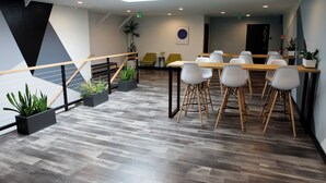 A modern conference room with a wooden floor, white chairs, and a long table. - Stay Classy Hostel (San Diego)