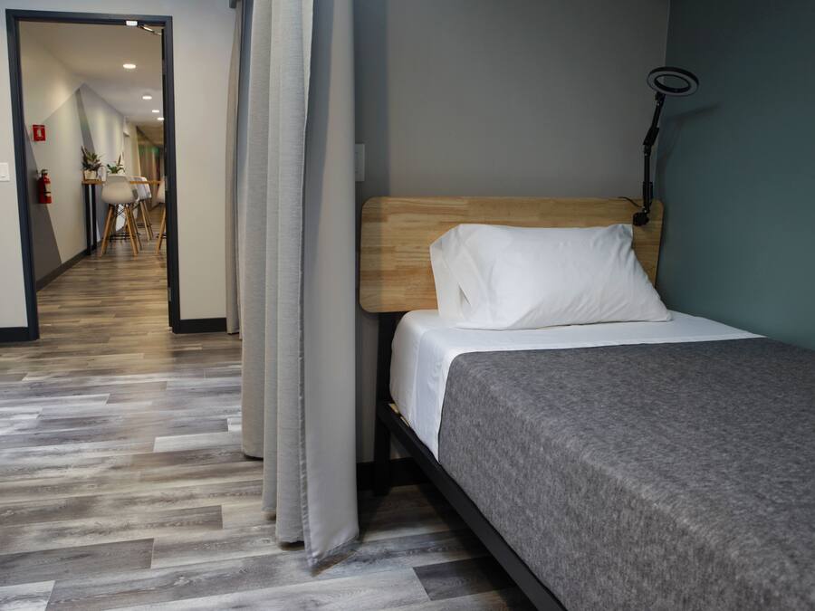 A hotel room with a bed, a desk, and a chair. There is a hallway leading to another room.