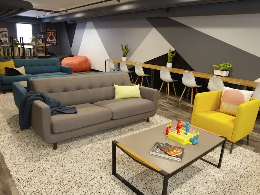 Un salon moderne avec un canapé gris, un fauteuil jaune et une table basse sur laquelle se trouvent un livre et des jouets.