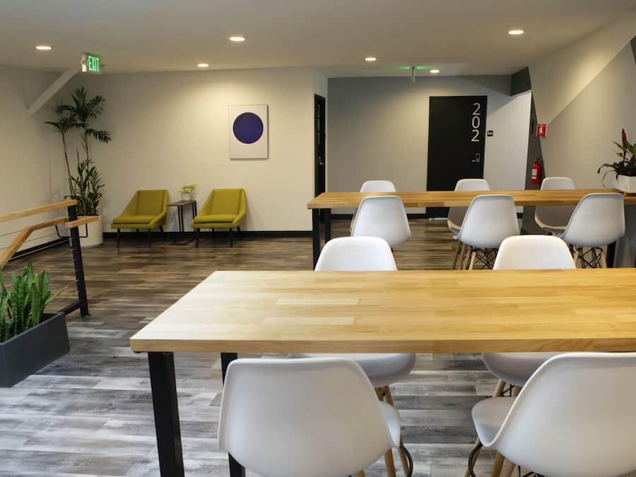 Une salle de conférence avec une longue table, des chaises blanches, une chaise jaune et une plante en pot.