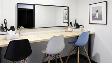 Een hotelkamer met een houten bureau, twee stoelen, een grote spiegel en kunstwerken in lijsten aan de muur.