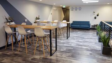 A modern conference room with a wooden table, white chairs, a blue sofa, and potted plants.