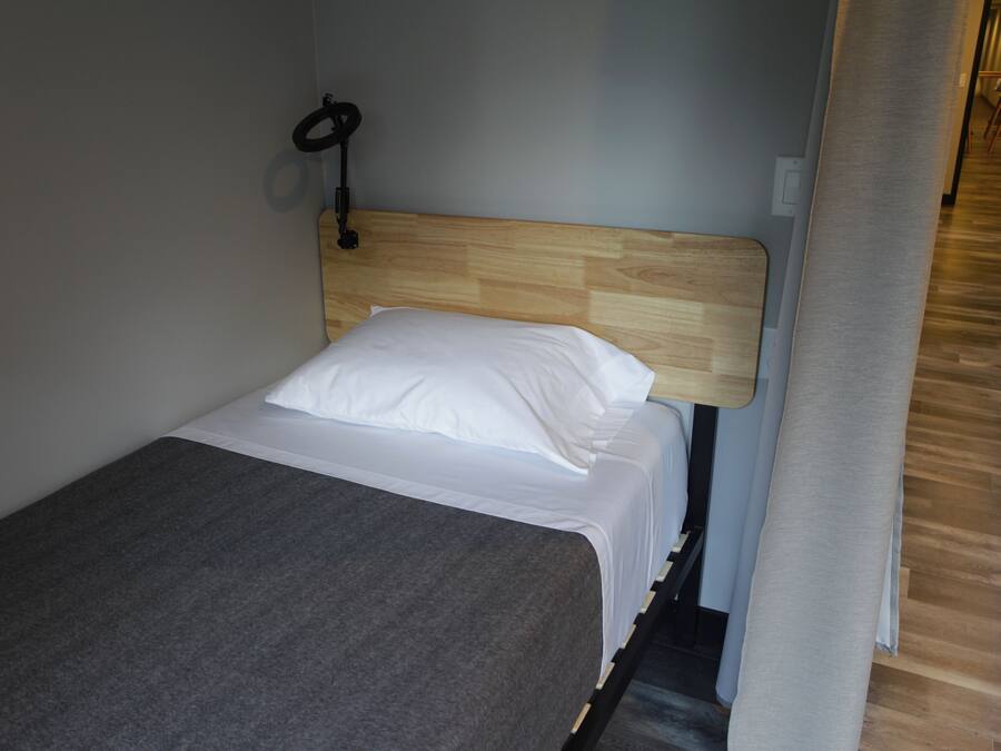 En lille, pænt opredt seng med et trægavl, et gråt tæppe og en hvid pude.