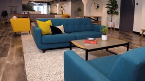 A modern lounge area with a blue sofa, yellow armchair, and a coffee table with a book and a potted plant. - Stay Classy Hostel (San Diego)