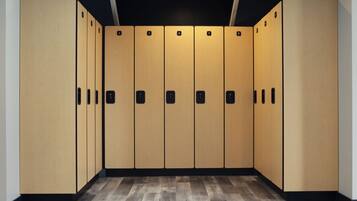 A row of wooden lockers with black handles and numbered doors, arranged in a hallway with a wooden floor.