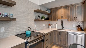 A kitchen with a brick backsplash, wooden cabinets, a stainless steel dishwasher, and a blue kettle on the stove. - Steps to Shopping, Restaurants, Year-Round Recreation & More! Park City Resort Village 208 (Park City)