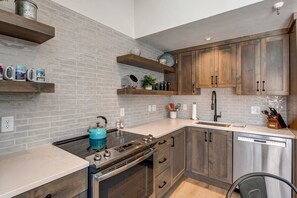 A kitchen with a brick backsplash, wooden cabinets, a stainless steel dishwasher, and a blue kettle on the stove.