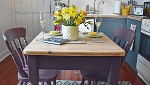 Une table à manger avec des chaises, un vase de fleurs, deux verres de vin blanc et un livre.