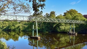 Un pont métallique enjambant une rivière paisible, bordée de part et d’autre par une végétation luxuriante.