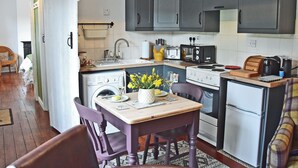 Une cuisine compacte équipée d’un évier, d’une cuisinière et d’un four à micro-ondes. On y trouve une table à manger avec des chaises et un vase de fleurs.