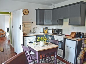 A compact kitchen with a sink, stove, and microwave. There is a dining table with chairs and a vase of flowers. - 1 bedroom accommodation in Thorngrafton, near Bardon Mill (Thorngrafton, near Bardon Mill)