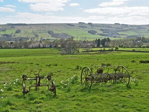 A rural landscape with rolling hills, a field with a vintage tractor, and a small building in the distance. - 1 bedroom accommodation in Thorngrafton, near Bardon Mill (Thorngrafton, near Bardon Mill)