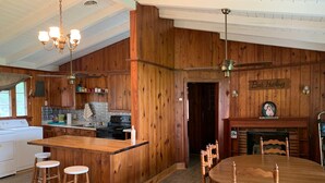 A wooden kitchen with a central island, bar stools, a dining table with chairs, and a ceiling fan. - Lakeside Retreat With Panoramic Views Like No Other (Lake Waccamaw)