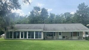 A single-story house with a covered patio area, large sliding glass doors, and a lawn in front. - Lakeside Retreat With Panoramic Views Like No Other (Lake Waccamaw)