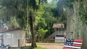 A grassy yard with a swing set, a wooden deck, and a house in the background. - Lakeside Retreat With Panoramic Views Like No Other (Lake Waccamaw)