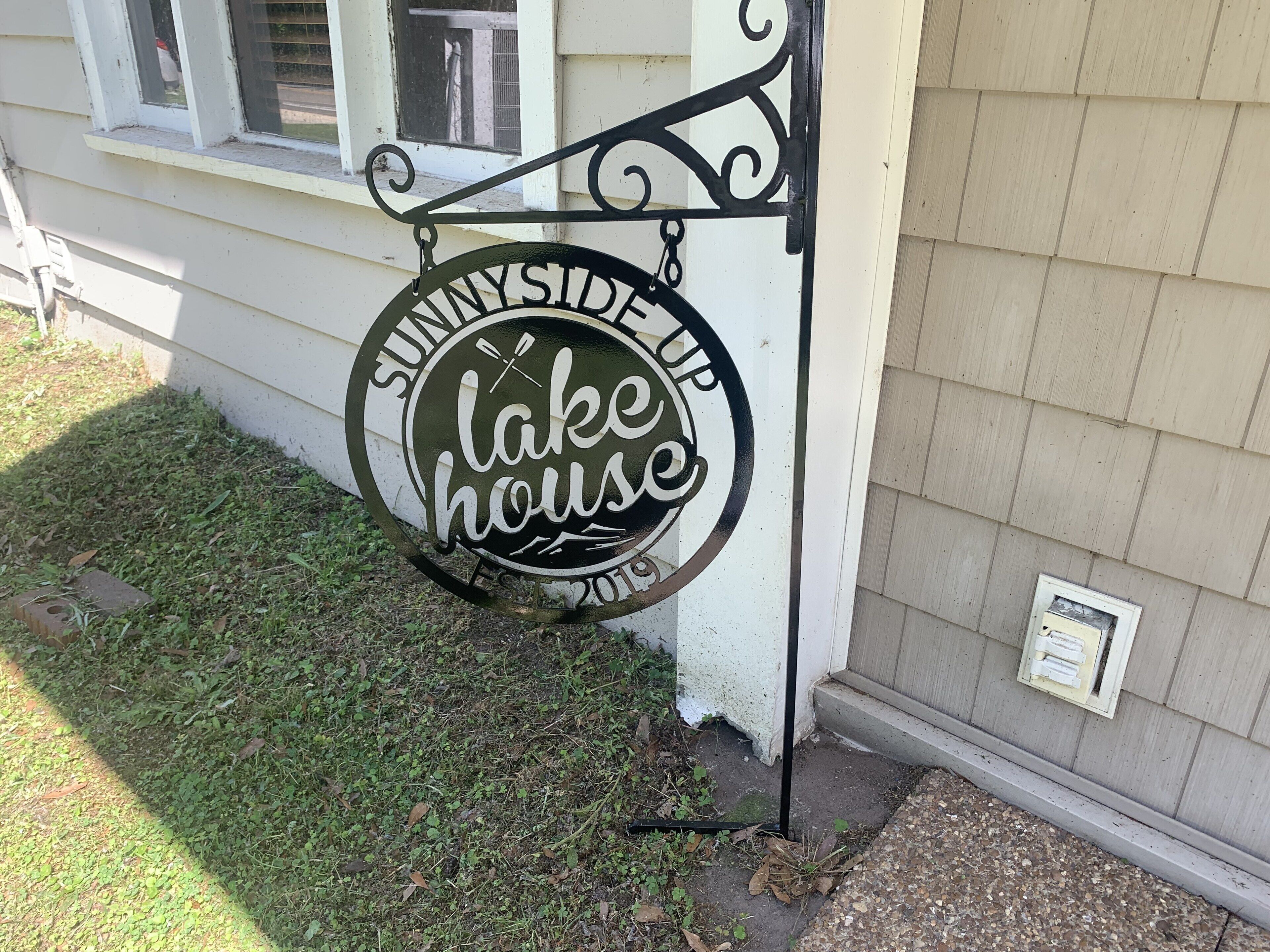 Een bord met de tekst 'SunnySideUp Lake House', voorzien van een decoratieve metalen lijst.