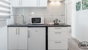 Una cocina moderna con armarios blancos, un microondas, una estufa y un lavaplatos. Hay dos cajones y una encimera con una olla encima.
