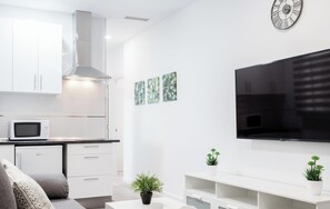 A modern kitchen with white cabinets, a microwave, and a large flat-screen TV mounted on the wall.