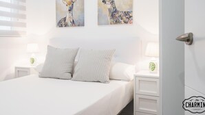 Un dormitorio con una cama, dos almohadas a rayas, una mesita de noche con una lámpara y dos cuadros de ciervos colgados en la pared.