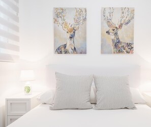 Une chambre à coucher comprenant un lit, deux tables de chevet, deux lampes et deux tableaux représentant des cerfs, accrochés au mur.
