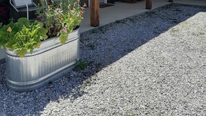 Un espacio al aire libre cubierto con un camino de grava, pilares de madera y plantas en macetas.