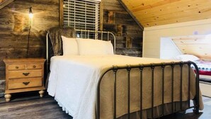 Un dormitorio con techo inclinado, un aparador de madera, una cama con estructura metálica y una ventana con persianas.