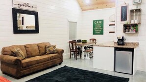Una sala de estar acogedora con un sofá marrón, un tapete negro y un comedor con una mesa y sillas de madera.