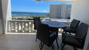 A balcony with a table and chairs, a ceiling fan, and a view of the ocean and a tall building. - Modern Oceanfront Hideaway, Ship Views & Steps to the Sand. Fort Lauderdale (Fort Lauderdale)