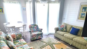 A living room with a green sofa, a floral armchair, a patterned rug, and a starfish rug. - 2024 Totally Renovated Oceanview condo Indoor/Outdoor Pool, 150' Waterslide Wifi (Atlantic Beach)