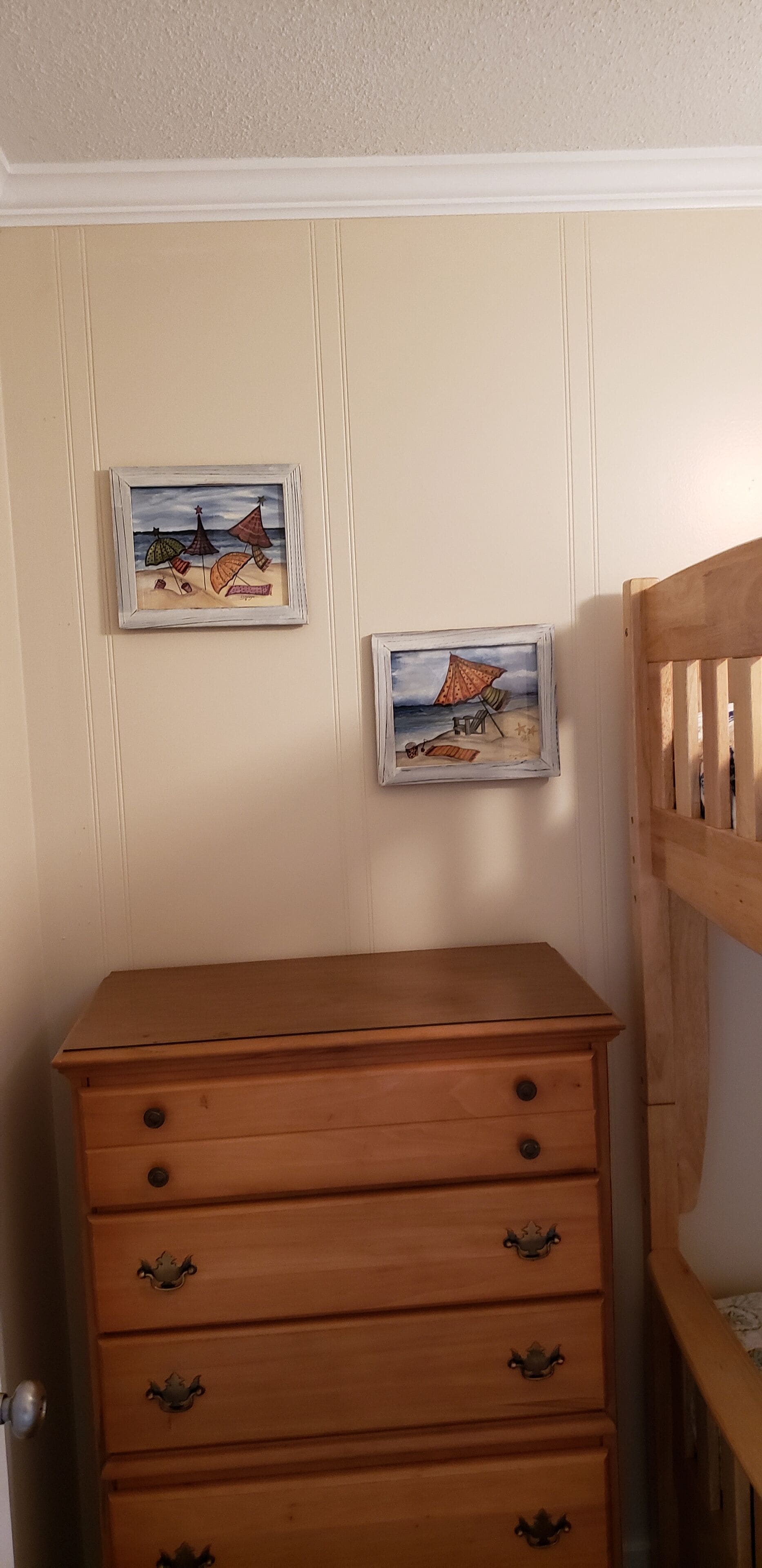 A wooden dresser with drawers and a small framed beach scene on the wall.
