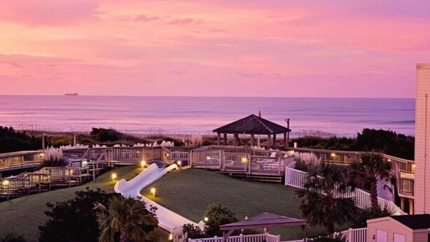 A resort with a pool, a gazebo, and a view of the ocean at sunset. - 2024 Totally Renovated Oceanview condo Indoor/Outdoor Pool, 150' Waterslide Wifi (Atlantic Beach)