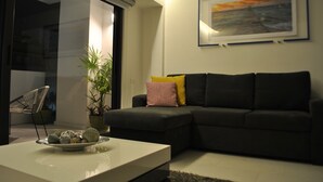 Un salon moderne avec un canapé foncé, une table basse agrémentée d’objets décoratifs, une plante en pot et un tableau encadré accroché au mur.