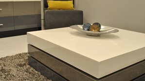 Un salon moderne avec une table basse blanche, un canapé gris agrémenté d’un coussin jaune et un bol décoratif posé sur la table.