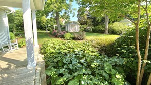 A covered porch with a rocking chair, a well-maintained garden with various plants and a small gazebo. - Downtown Manteo with Secret Garden (Manteo)