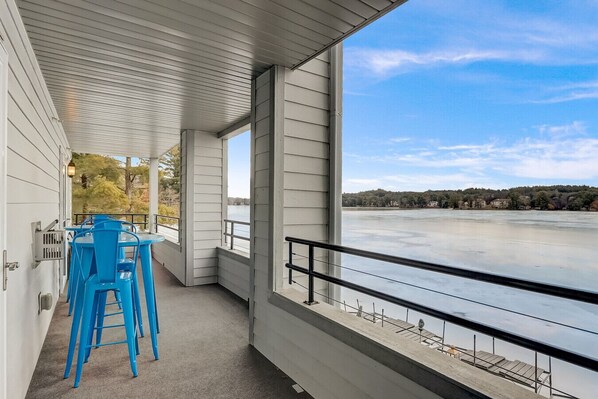 A covered outdoor area with a table and chairs, overlooking a body of water and a distant shoreline.