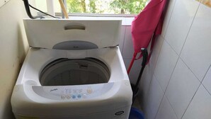 A front-loading washing machine with a control panel, located in a room with tiled walls and a window.