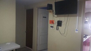 A room with a closed door, a small table with papers, a mounted telephone, and a TV on the wall.
