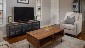 A living room with a TV, wooden coffee table, armchair, and shelving unit.