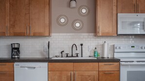 A modern kitchen with wooden cabinets, a white tiled backsplash, a stainless steel coffee maker, a sink with a faucet, a microwave, and a dishwasher.