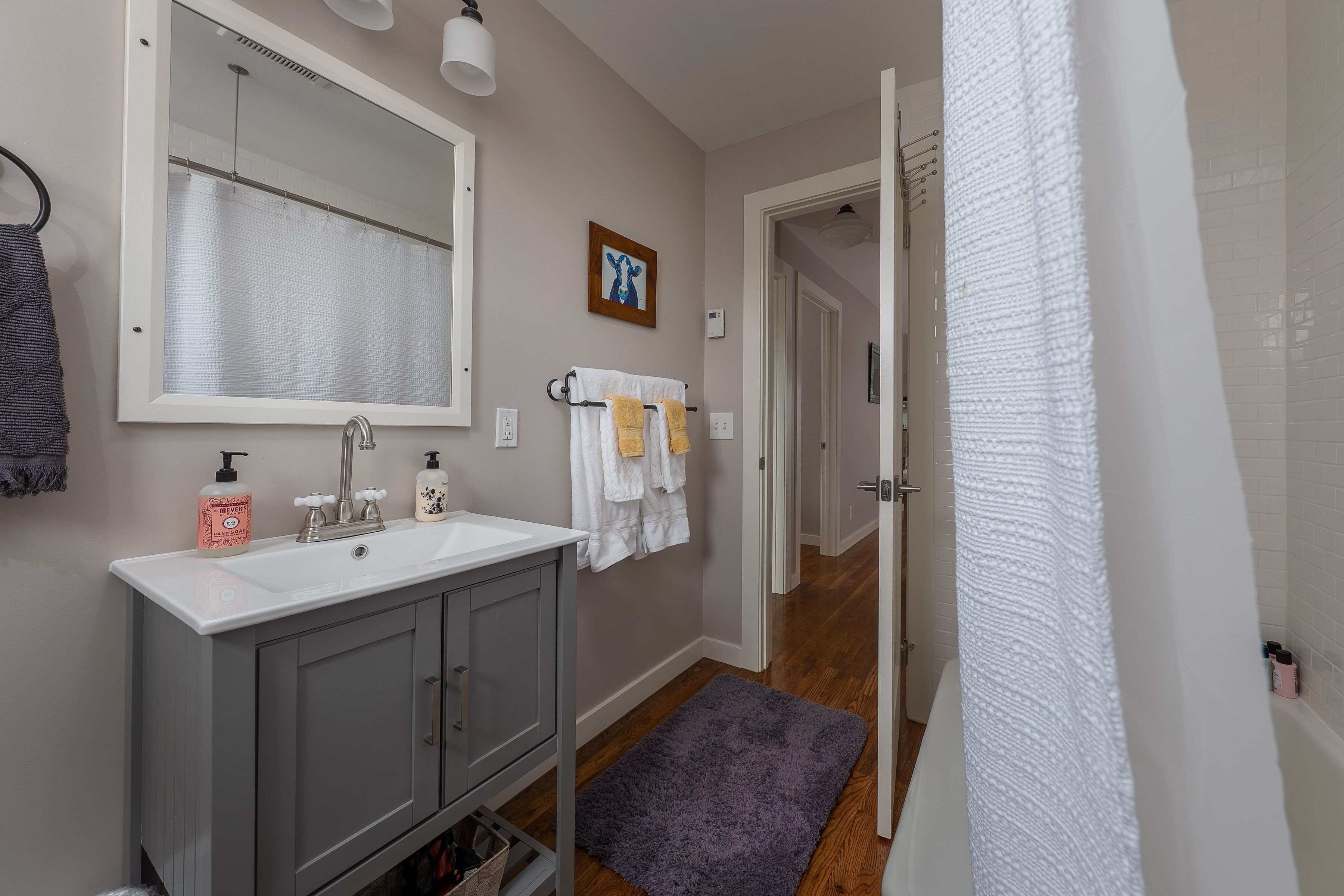 Un baño con lavamanos blanco, espejo y toallero.