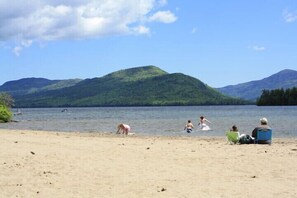 Une plage où l’on peut voir des gens pratiquer diverses activités, un ciel dégagé et des montagnes en arrière-plan.