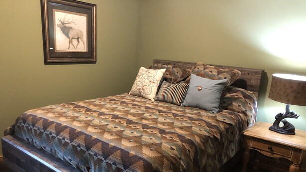 Quarto com colcha estampada, quadro de um veado na parede e mesa de cabeceira com abajur.